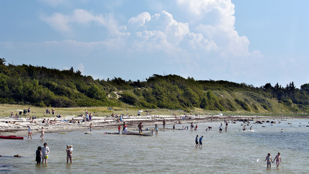 Badegæster og både ved Kulhuse Strand med grønne skrænter i baggrunden.
