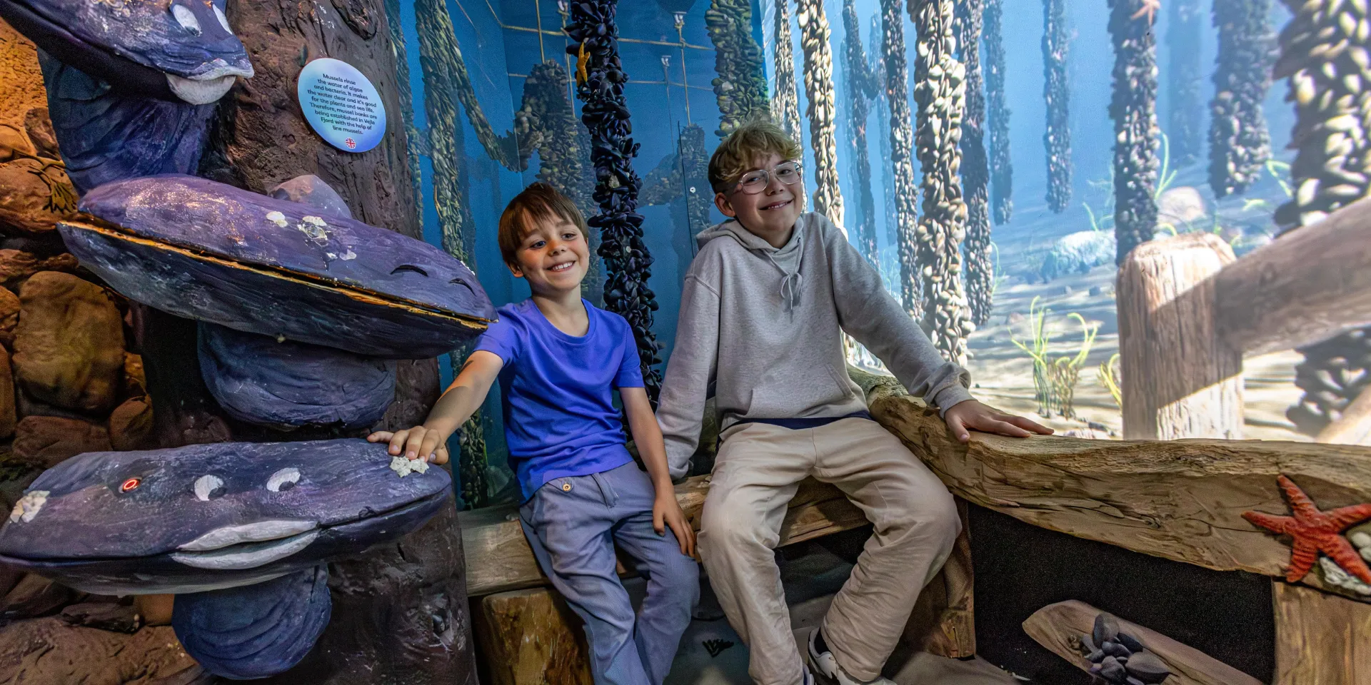 Children sit on the seabed among large and small mussels in the exhibition "Seabed and Fjord".