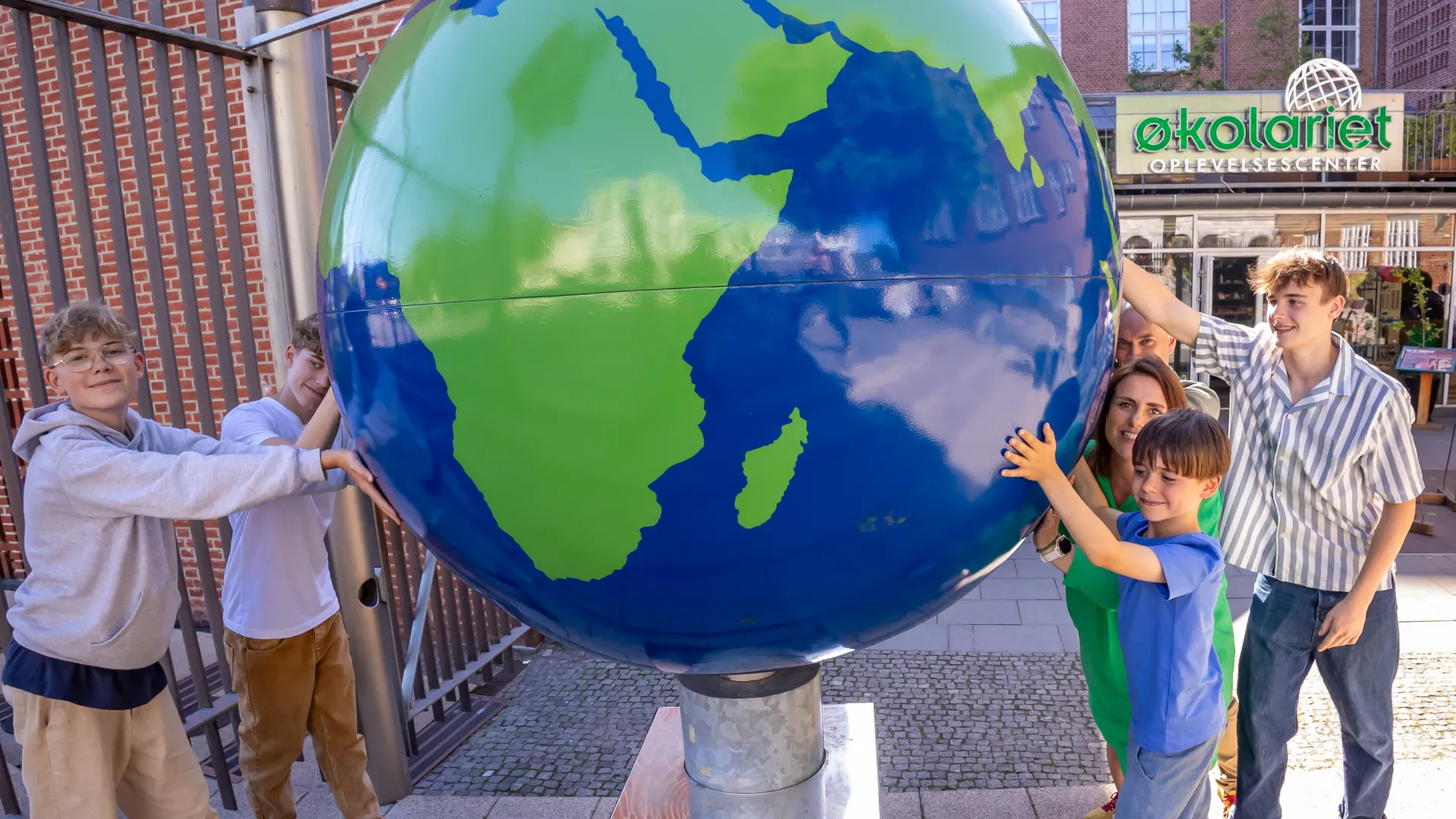 Children and mother stand in front of the entrance by the large globe outside in front of the Ecolarium
