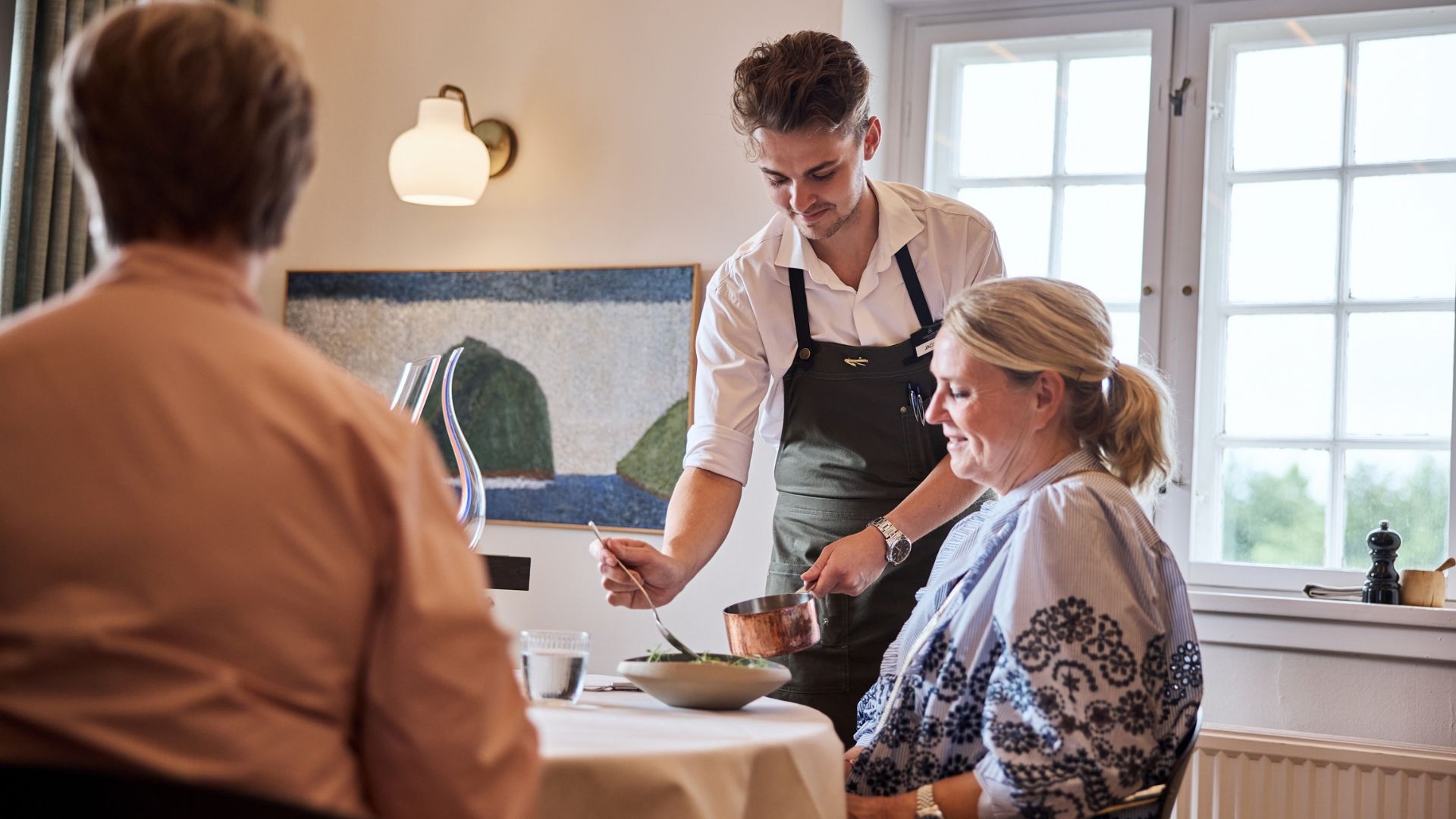 En tjener serverer middag til kvinder siddende ved et bord i restauranten ved Haraldskær i Vejle