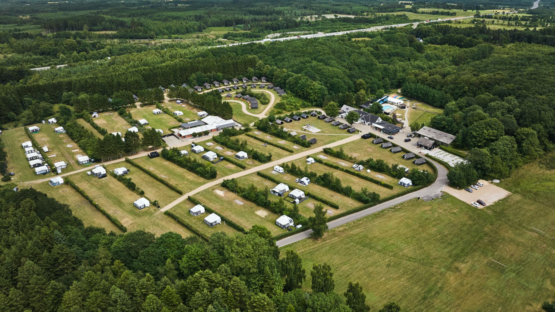 Riis Feriepark in Give aus der Vogelperspektive, umgeben von Wald und mit einem Freibad.
