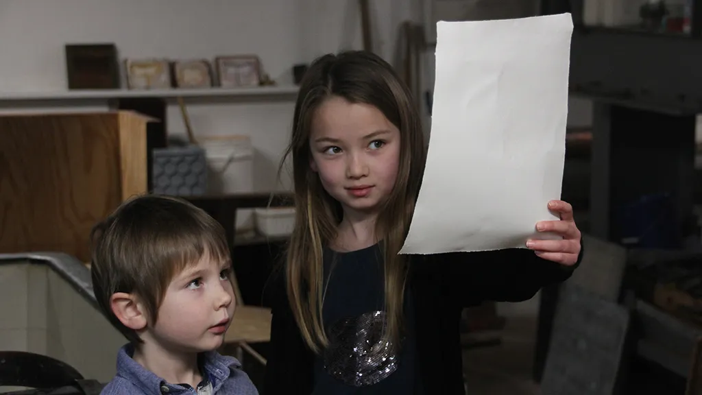To børn kigger på et stykke papir på Papirmuseet
