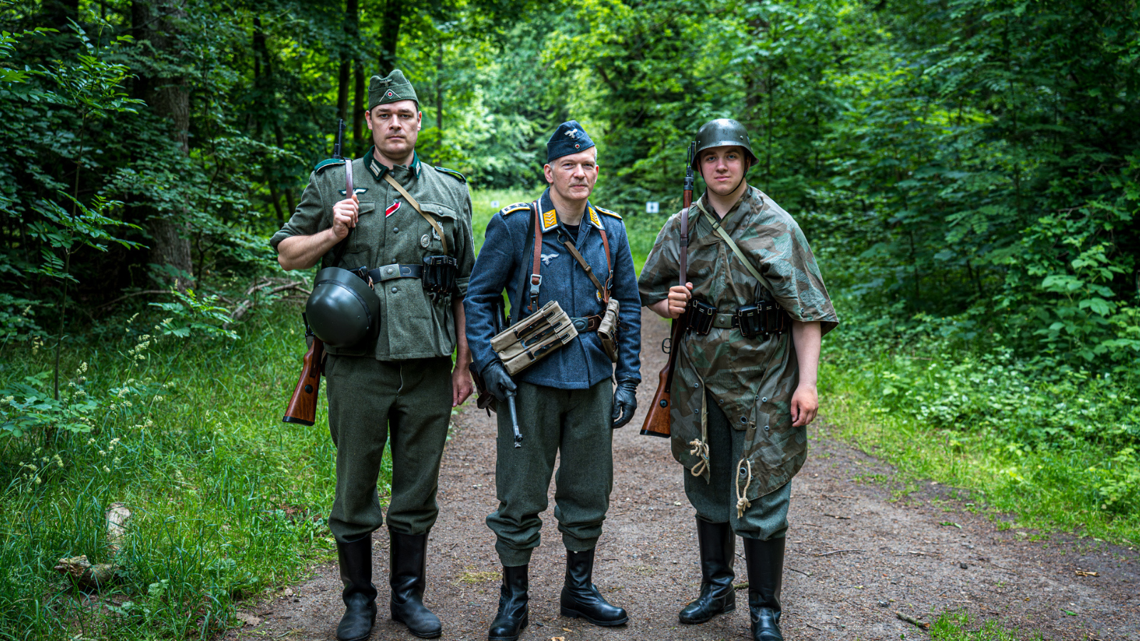 Tre mænd der står ude i naturen udklædt i militær tøj.