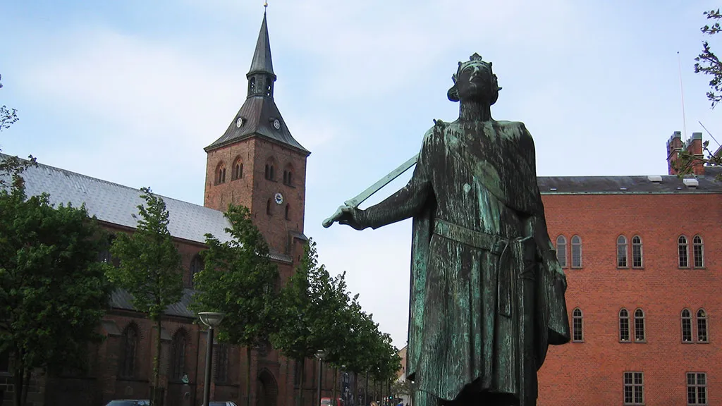 Bronze sculpture in front of red buildings with towers and spires.
