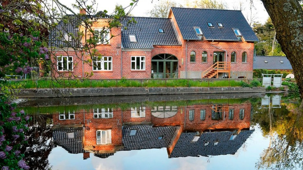 Red building with black roof reflected in the water.