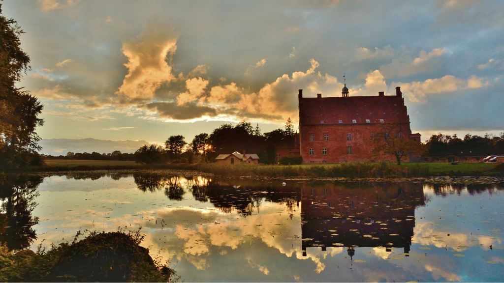 Stor rød bygning spejler sig i vandet.