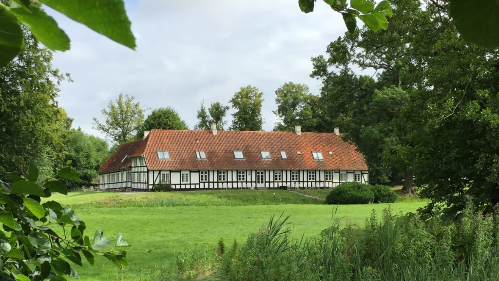 Hvid herregård med bindingsværk og rødt tag ses på afstand.