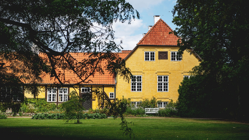 Large yellow farm with a red roof in cozy natural surroundings.