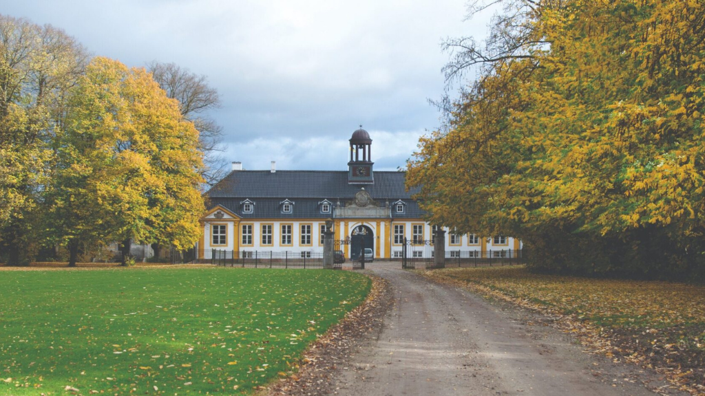 Yellow castle with black roof and a bell tower can be seen in the distance with a road leading up to the entrance.