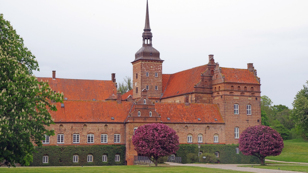 Large red castle with red roof and colorful bushes in front.