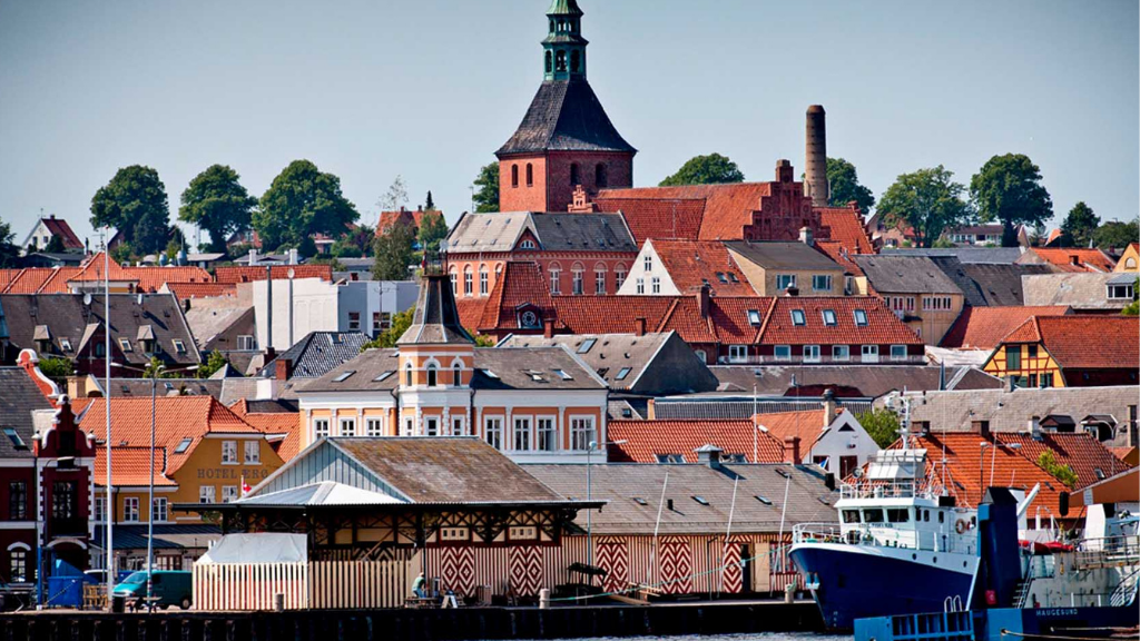 A town with close-knit, colorful houses with many red roofs and a church tower that stands out in the middle.