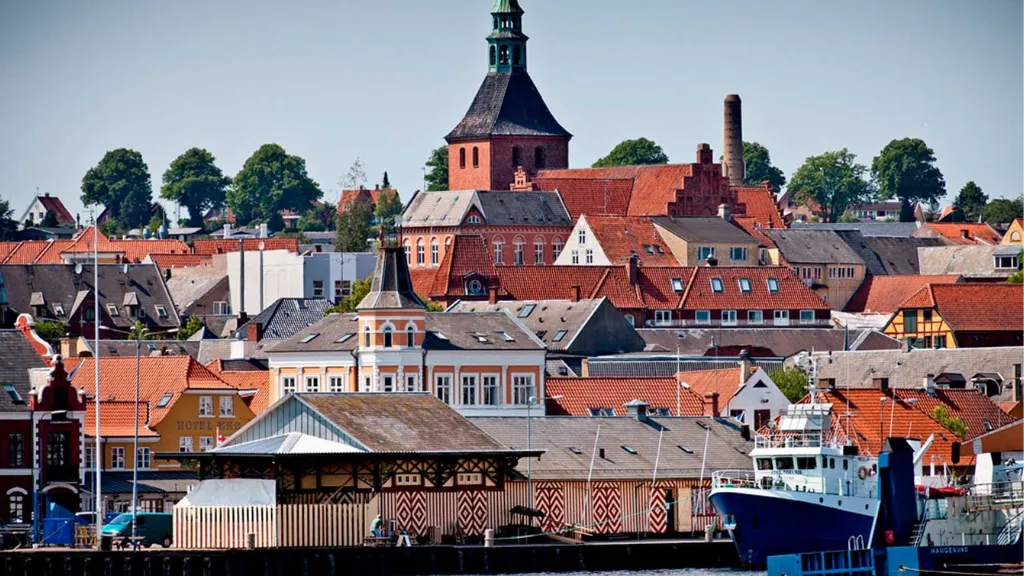 By med tætliggende, farverige huse med mange røde tage og et kirketårn, der stikker op i midten.