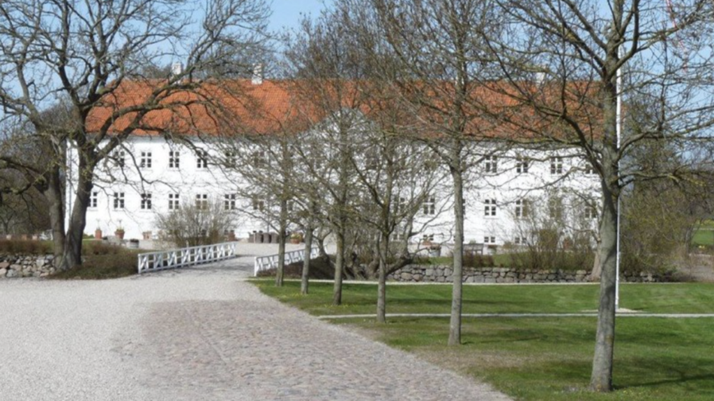 Stor, hvid herregård med rødt tag og en vej, der fører op til den.