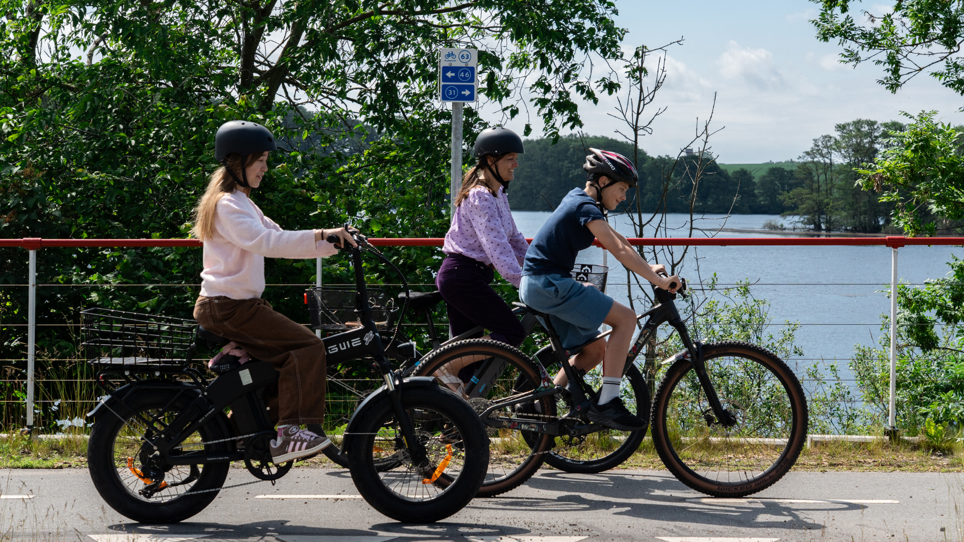 Cyclists riding on a path with a cycling node network sign in the background.